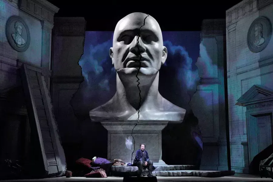 A giant bust of a man looms over two actors on stage in a production of Don Giovanni 在威尼斯人官网平台app.