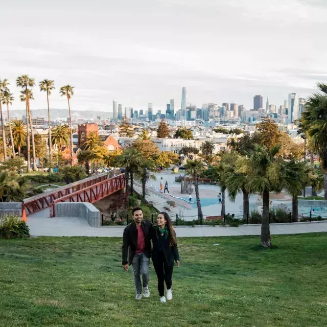 Una pareja camina hacia la cámara con Dolores Park y el Skyline 威尼斯人官网平台app detrás de ellos.